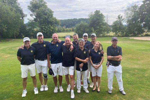 Zehn Personen in dunkelblauen Poloshirts und weißen Hosen stehen lächelnd zusammen auf einem Golfplatz