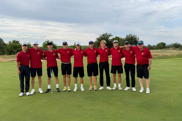 Elf Personen in roten Poloshirts und dunklen Hosen stehen auf einem Golfplatz nebeneinander und legen die Arme umeinande