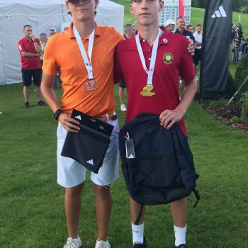 Acht Männer in dunkelblauen Poloshirts und weißen Hosen oder Shorts posieren auf einem sonnigen Golfplatz; einige stehen, andere knien davor. (Text erstellt mit Hilfe von KI.)