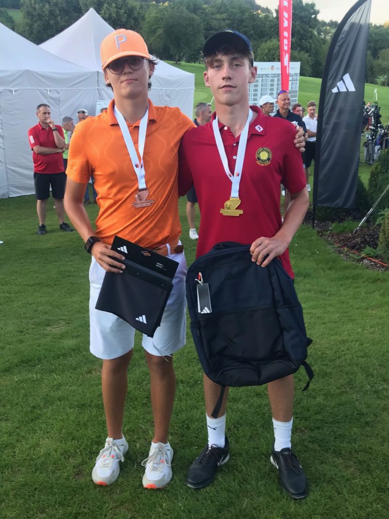 Acht Männer in dunkelblauen Poloshirts und weißen Hosen oder Shorts posieren auf einem sonnigen Golfplatz; einige stehen, andere knien davor. (Text erstellt mit Hilfe von KI.)