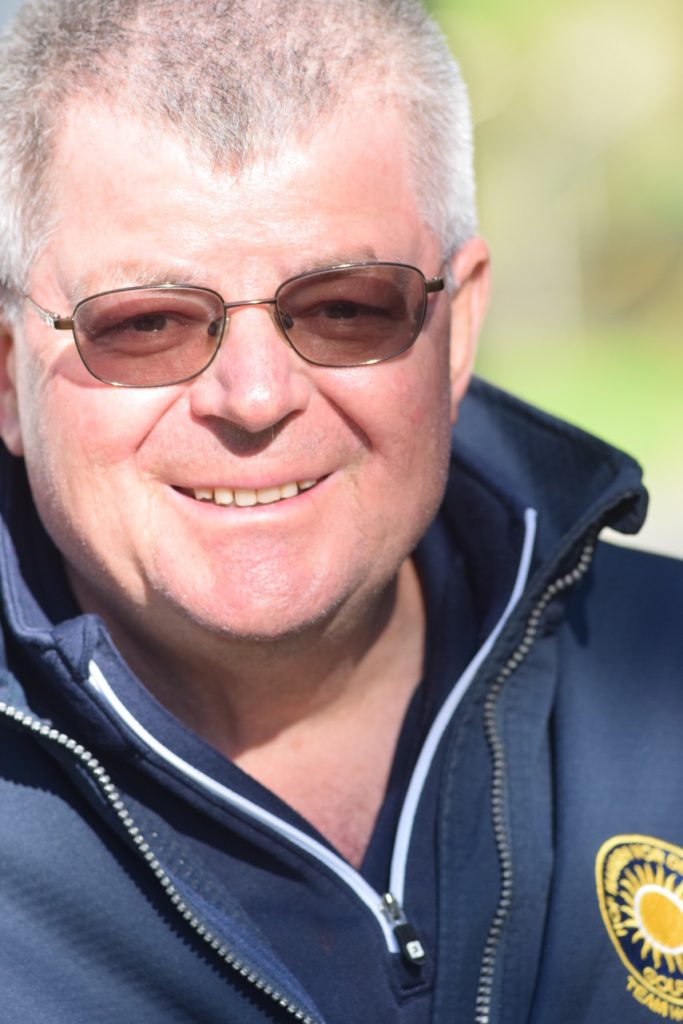 Lächelnde Person mit Brille in dunkler Jacke im Freien