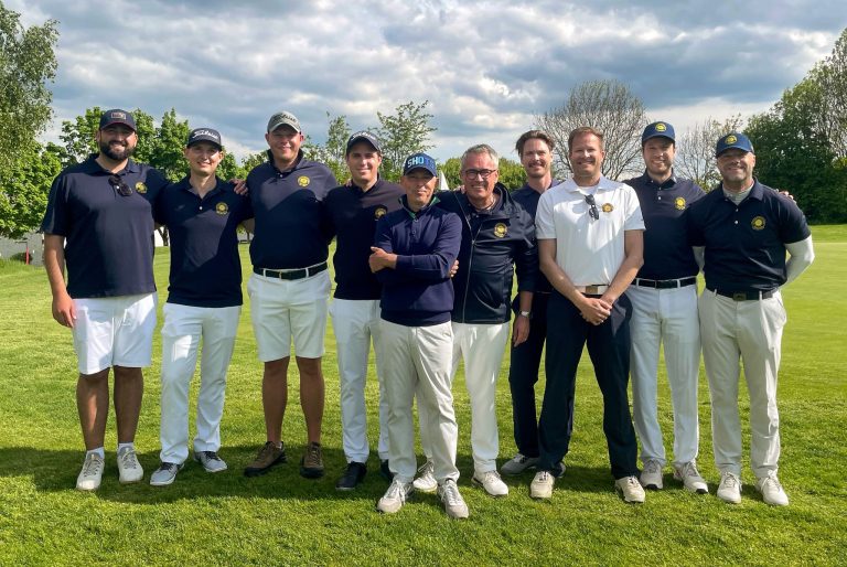Eine Gruppe von 10 Männern in einheitlicher Golfkleidung steht nebeneinander auf einem Golfplatz und lächelt in die Kamera.