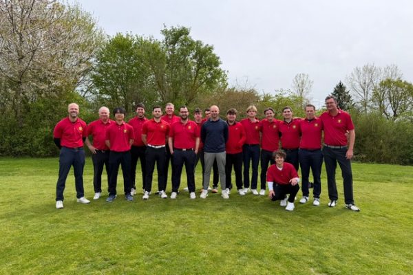 Gruppe von Männern in roten Poloshirts steht gemeinsam auf einer Wiese im Freien und blickt in die Kamera.