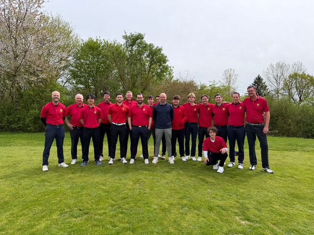 Gruppe von Männern in roten Poloshirts steht gemeinsam auf einer Wiese im Freien und blickt in die Kamera.