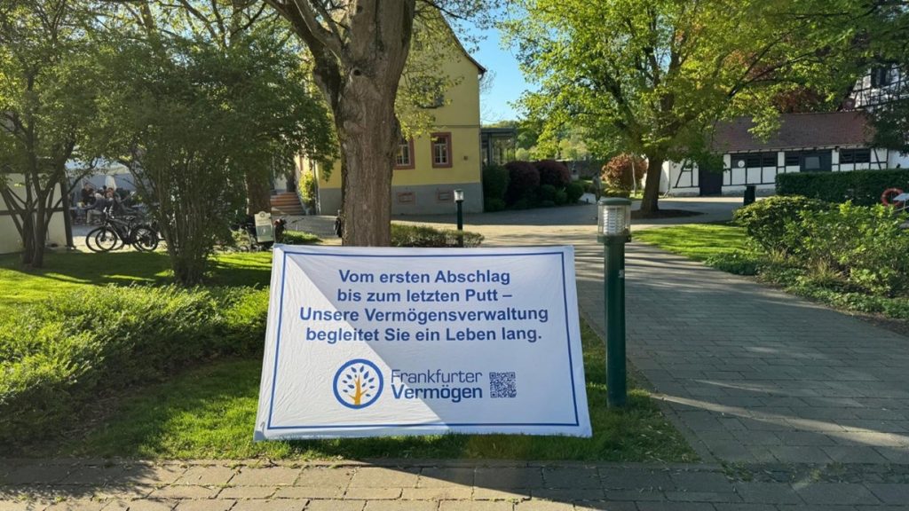 Werbebanner eines Vermögensverwalters auf einem gepflegten Gelände mit Bäumen und Gebäuden im Hintergrund.