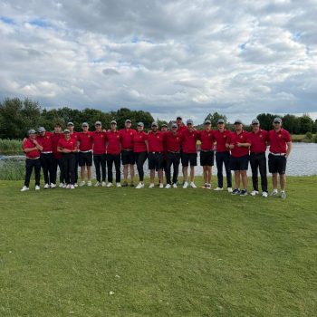 Die Jugendmannschaften des Golf Club Hof Hausen vor der Sonne versammeln sich gemeinsam mit ihren Trainerinnen und Trainern für ein Gruppenfoto auf dem Golfplatz. Alle tragen einheitliche rote Poloshirts mit Clublogo.