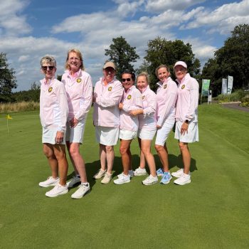 Die Damenmannschaft des Golf Club Hof Hausen vor der Sonne posiert gemeinsam auf dem Putting Green. Die Spielerinnen tragen einheitliche rosafarbene Teamjacken und weiße Röcke bzw. Shorts