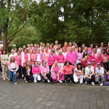 Gruppenfoto von rund 70 Damen des Golf-Club Hof Hausen in pinker Kleidung beim Pink-Ribbon-Golftag. Sie stehen und knien vor grünen Bäumen auf dem Vorplatz der Anlage.