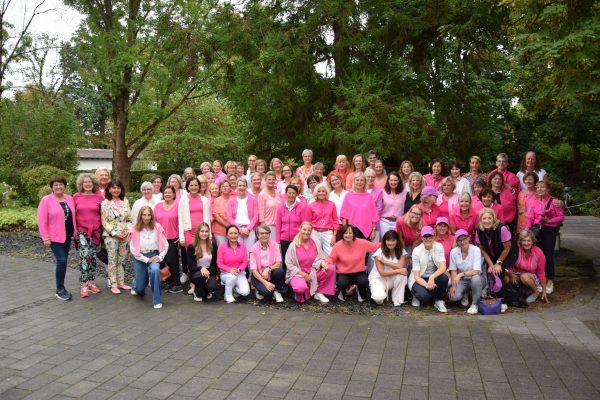 Gruppenfoto von rund 70 Damen des Golf-Club Hof Hausen in pinker Kleidung beim Pink-Ribbon-Golftag. Sie stehen und knien vor grünen Bäumen auf dem Vorplatz der Anlage.