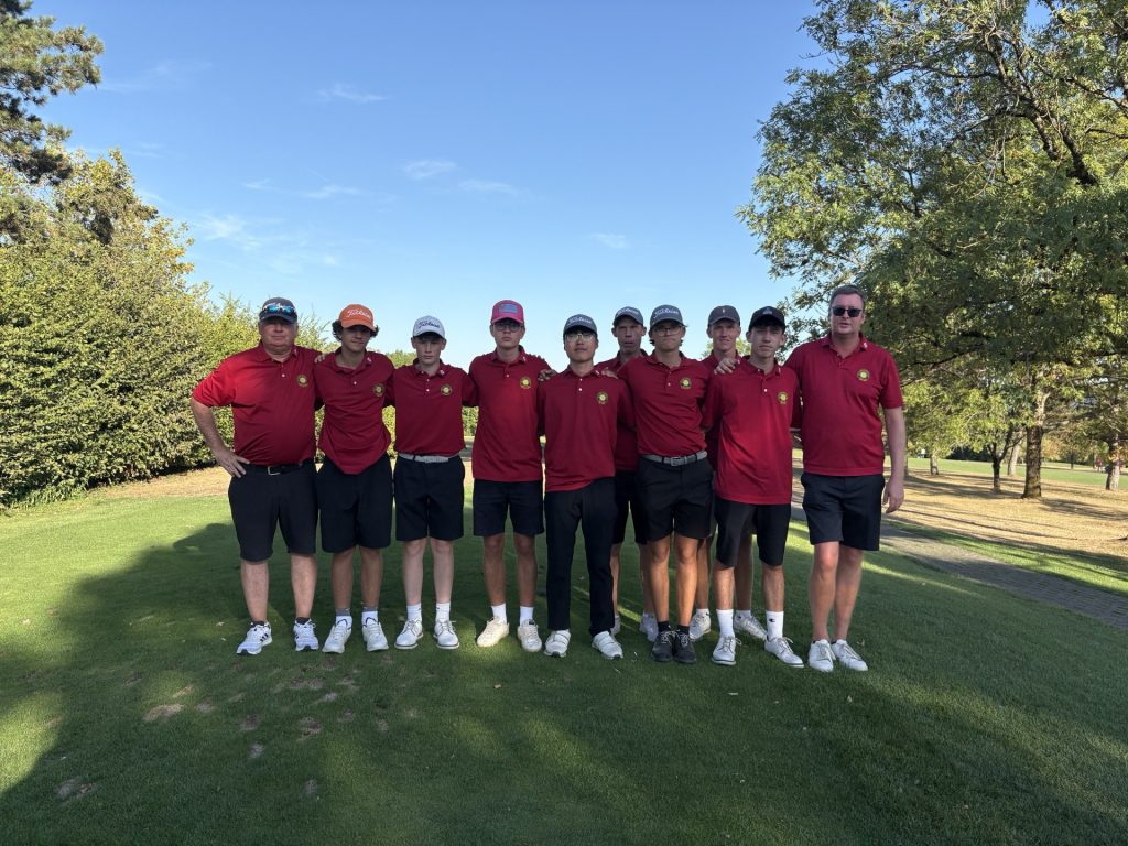 „Jugendmannschaft mit Trainern in roten Clubshirts auf einem Golfplatz.“