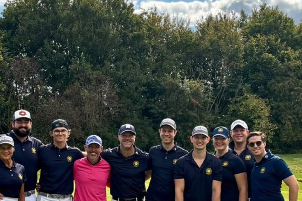 Mannschaftsfoto des Golfclubs Hof Hausen: zwölf Golferinnen und Golfer in dunkelblauen Clubshirts stehen lächelnd auf dem Grün vor hohen Bäumen.